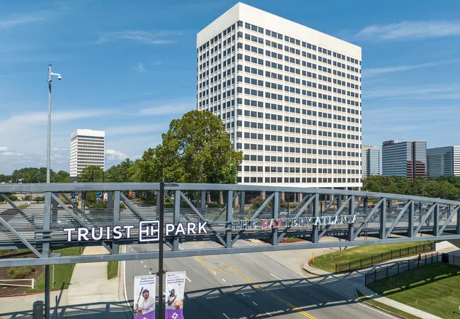 Modern pedestrian bridge with Truist Park and The Battery Atlanta signs in front of tall office buildings under blue sky
