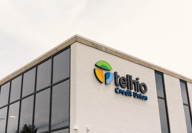 Telhio Credit Union logo on white brick building with large tinted windows under overcast sky.