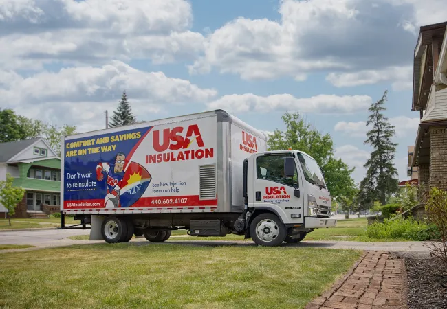 USA Insulation truck parked in a suburban neighborhood delivering home insulation services under a blue sky with clouds.