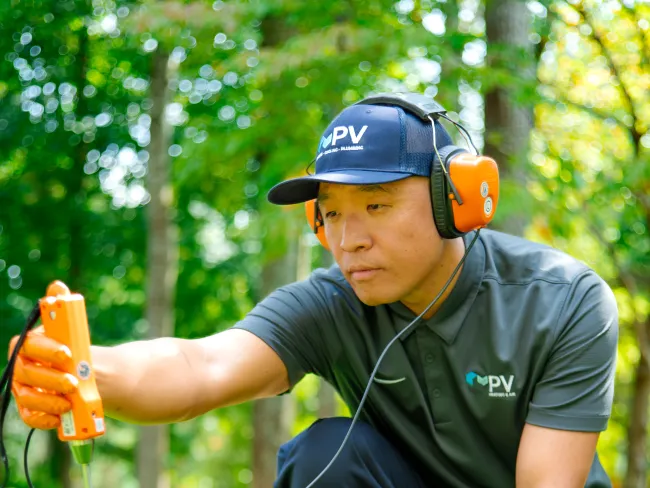 Man in uniform using soil testing tool on green grass wearing ear protection and orange gloves in park setting