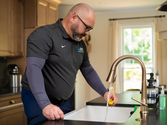 Technician testing water flow from kitchen faucet using a yellow tool in a modern kitchen sink area.