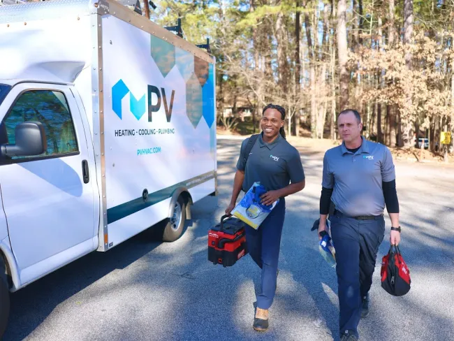 Two HVAC technicians walking towards a service van, ready for a job on a sunny day.