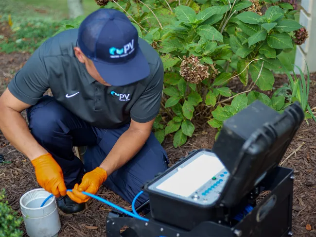 Technician in uniform kneeling outdoors connecting blue fiber optic cables to testing equipment.