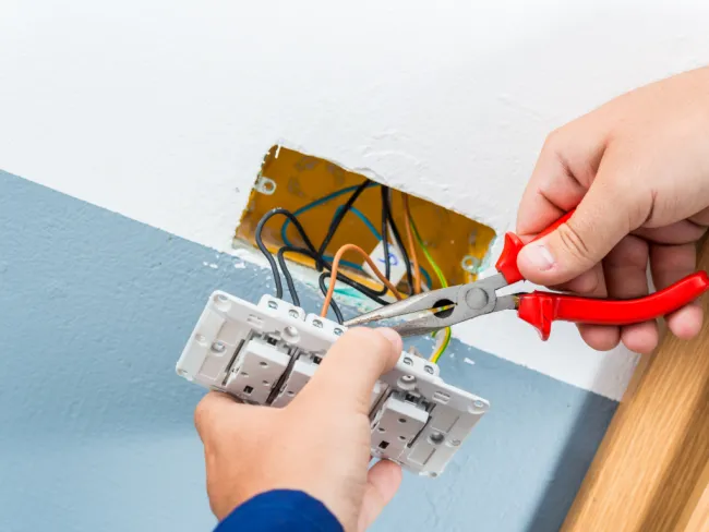 A person using pliers to manipulate electrical wires in a wall switch installation.