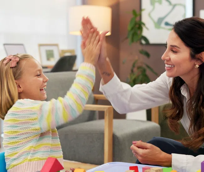 Smiling child and woman giving high five while playing with colorful wooden blocks at home.