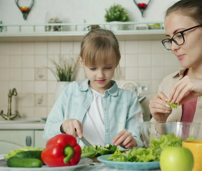 Mother and daughter preparing fresh salad together in bright kitchen with vegetables on table