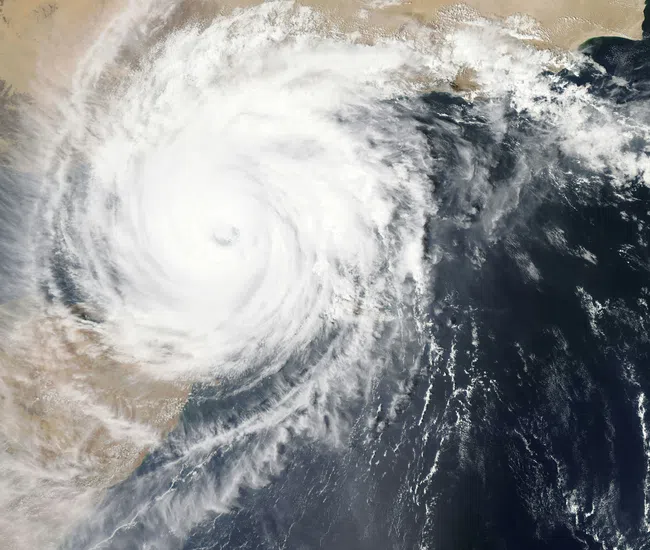 Satellite view of a large cyclone with a clear eye over ocean near a desert coastline, no overlaid text.