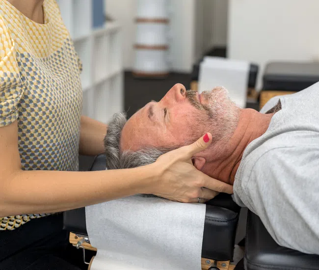 Chiropractor performing neck adjustment on middle-aged man lying on treatment table in clinic
