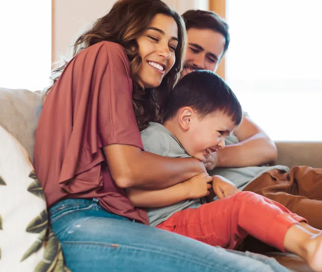 Happy family laughing and playing together on a cozy living room couch in natural light