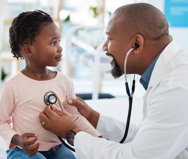 Doctor using stethoscope to examine young girl patient in bright medical office