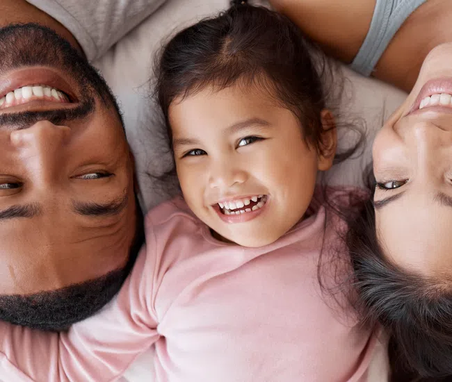 Smiling young family lying on bed with child in the center enjoying happy moments together.