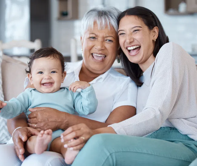 Happy multi-generation family with baby sitting on couch smiling brightly in a cozy living room.