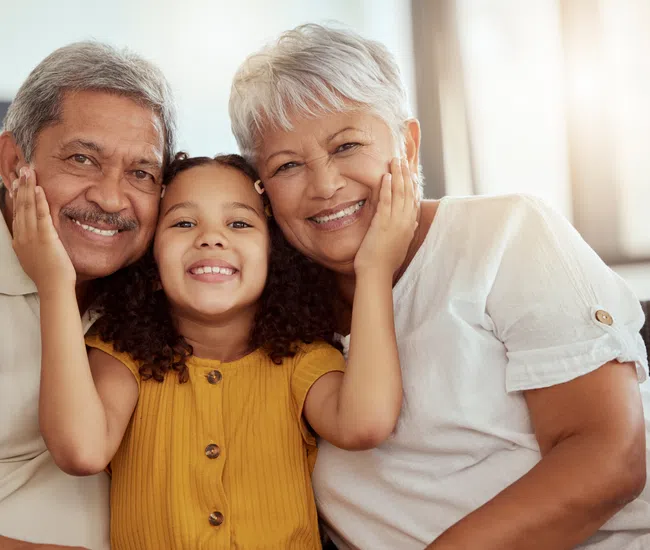 Smiling young girl hugs her grandparents, showing affection and warmth in a cozy home setting.