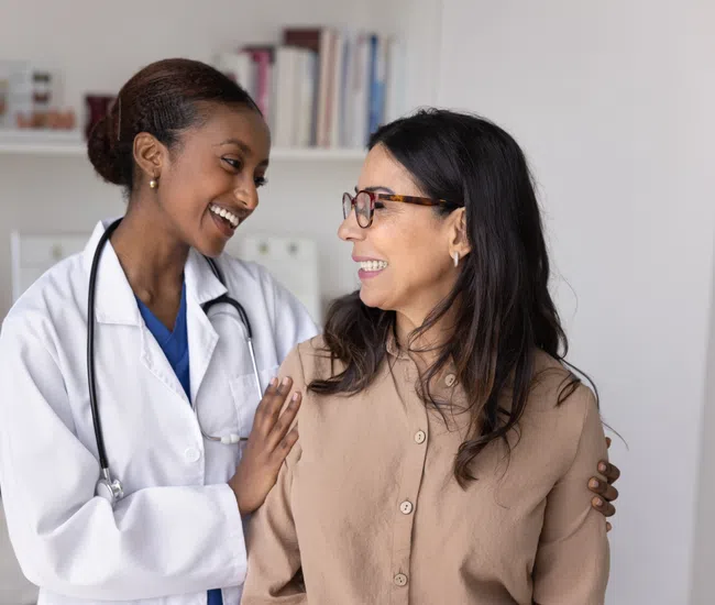 Smiling female doctor in white coat comforting a happy female patient in a medical office setting