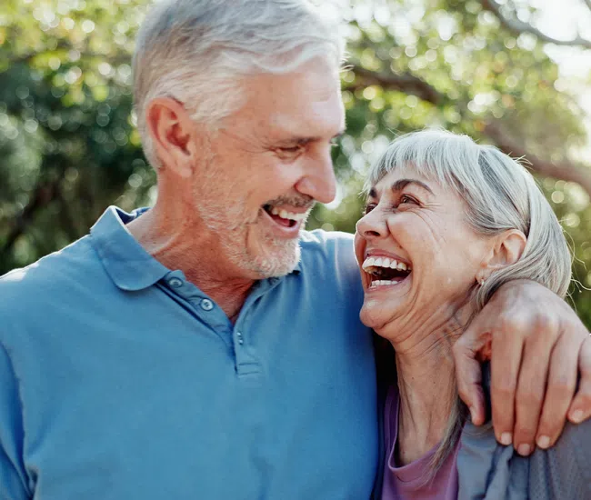 Happy senior couple embracing and laughing together outdoors in a sunlit garden setting.