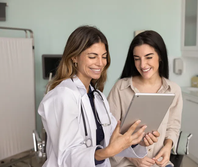 Female doctor showing medical information on tablet to a smiling patient in a clinic room