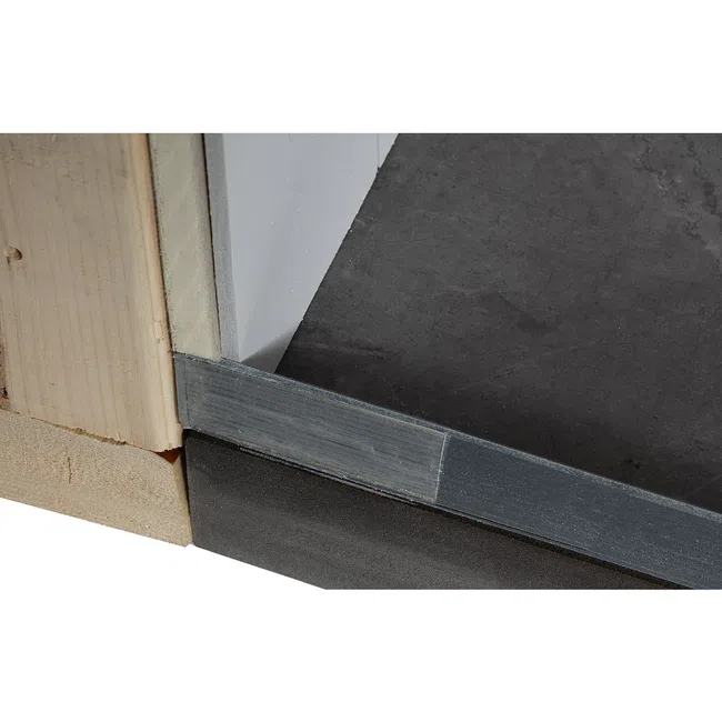 Close-up of a doorway threshold showing wood framing, door jamb, and metal strip on a dark floor.