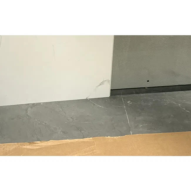 Close-up of marble and gray stone tiles meeting cardboard edge on floor with white and gray wall surfaces