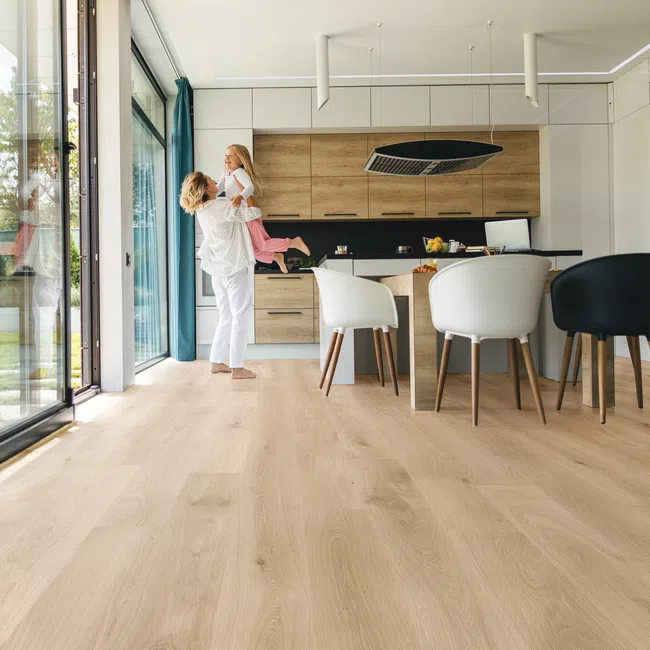 Mother lifting daughter in modern kitchen with light wood floor and large glass windows