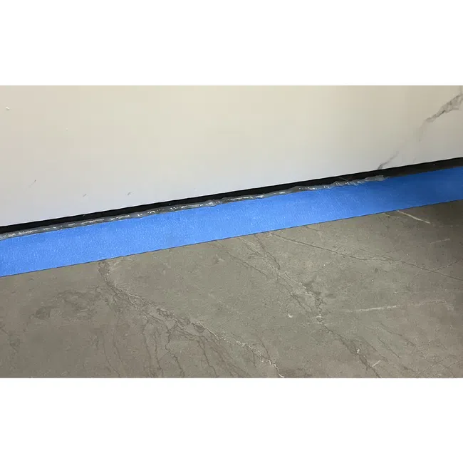 Blue painter's tape applied at the base of a white wall above a gray marble floor during room preparation.