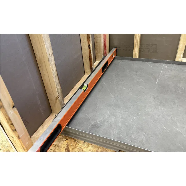 Orange spirit level placed on gray tiled floor next to wooden framed wall under construction.