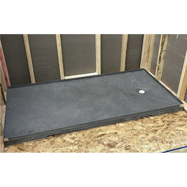 Black rectangular shower base installed on wooden floor with exposed wall studs in construction site.