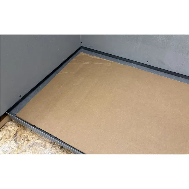Corner of an unfinished room with a cardboard sheet on the floor next to exposed plywood and gray walls.
