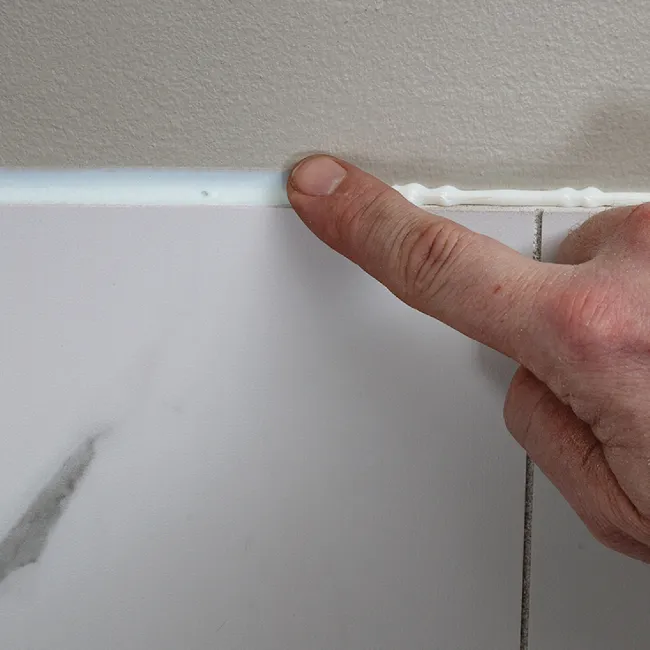 Close-up of finger smoothing fresh white tile adhesive above marble tile on wall during installation