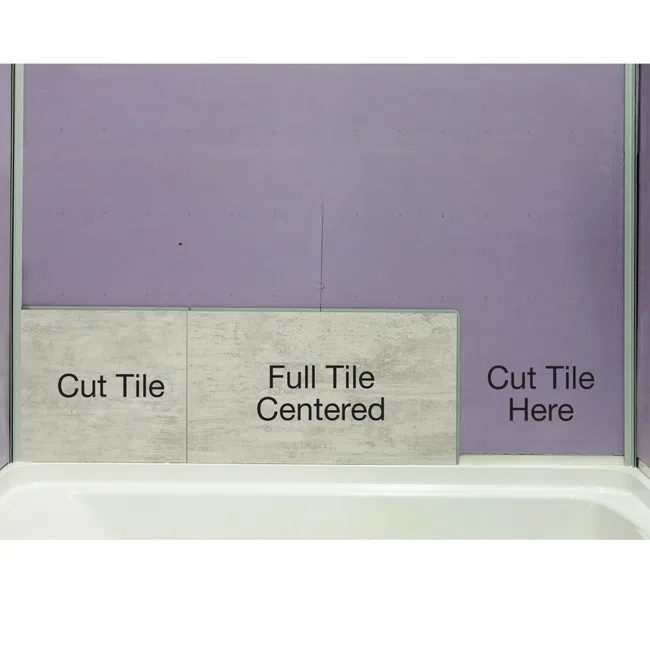 Bathroom wall showing tile placement with instructions for cut and full centered tiles above bathtub edge.