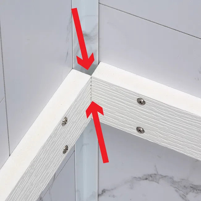 Closeup of white wooden frame corner joint with screws and red arrows on marble tile background