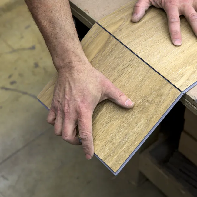 Hands aligning two wood laminate flooring panels on a table for installation or fitting.