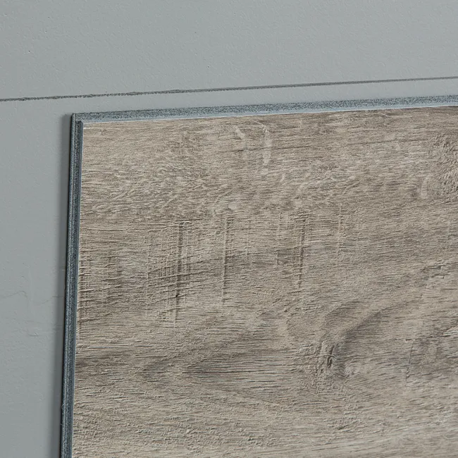 Close-up of a grayish wood floor panel with textured grain and a gray wall background.
