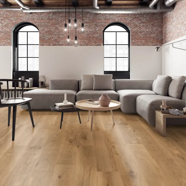 Modern living room with brick walls, large arched windows, gray sectional sofa, black chair, and wooden flooring