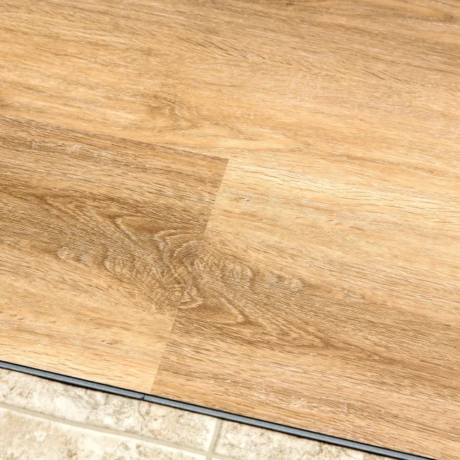 Close-up of wood laminate flooring joining tiled floor with a black transition strip between them.