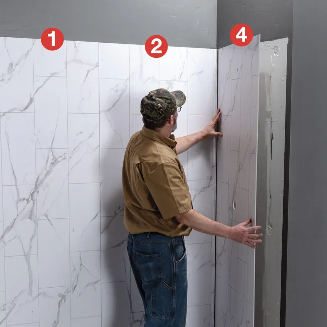 Man installing large marble-patterned wall panels in a room with gray walls and ceiling.