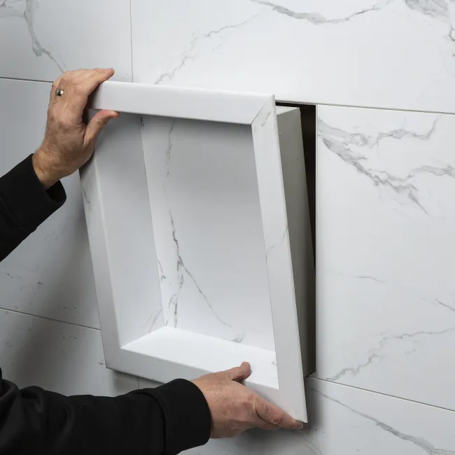 Person installing a white recessed wall niche with marble-patterned tiles surrounding the opening.