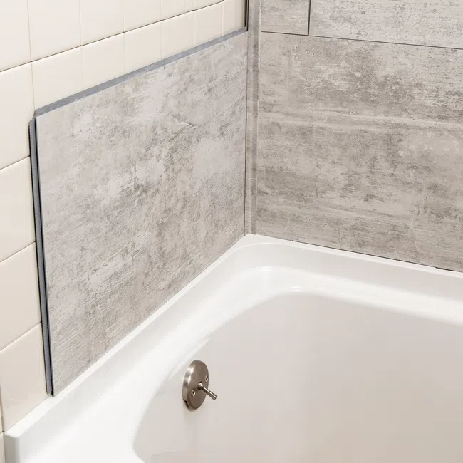 Close-up of bathtub corner with beige ceramic and gray stone-patterned wall tiles and a silver drain stopper.