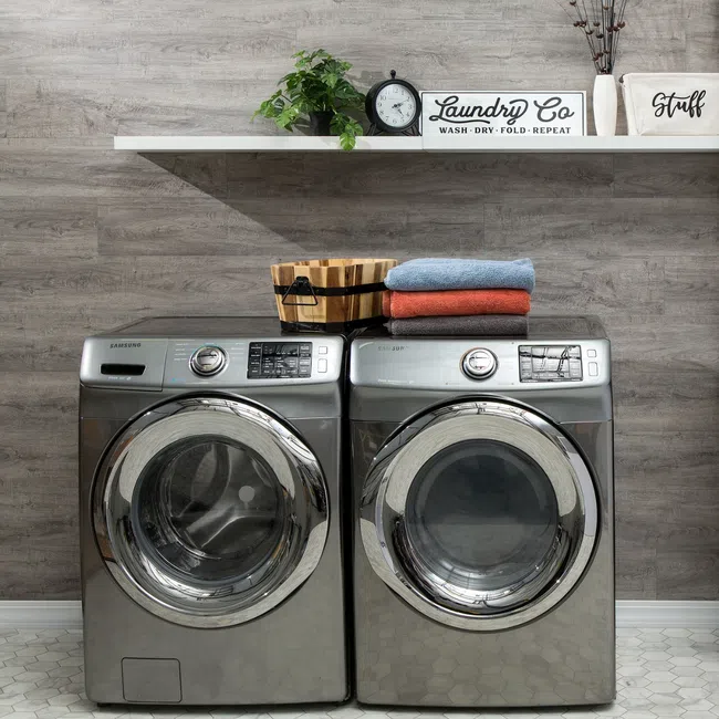 Modern laundry room with front-load washer and dryer, towels, sink, and decorative shelf with plants and signs