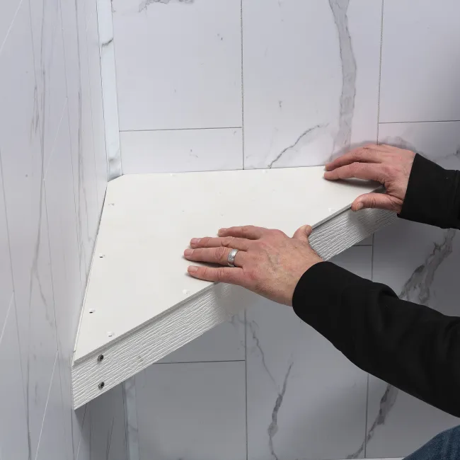 Person installing a white triangular wall shelf against a marble tiled wall indoor.