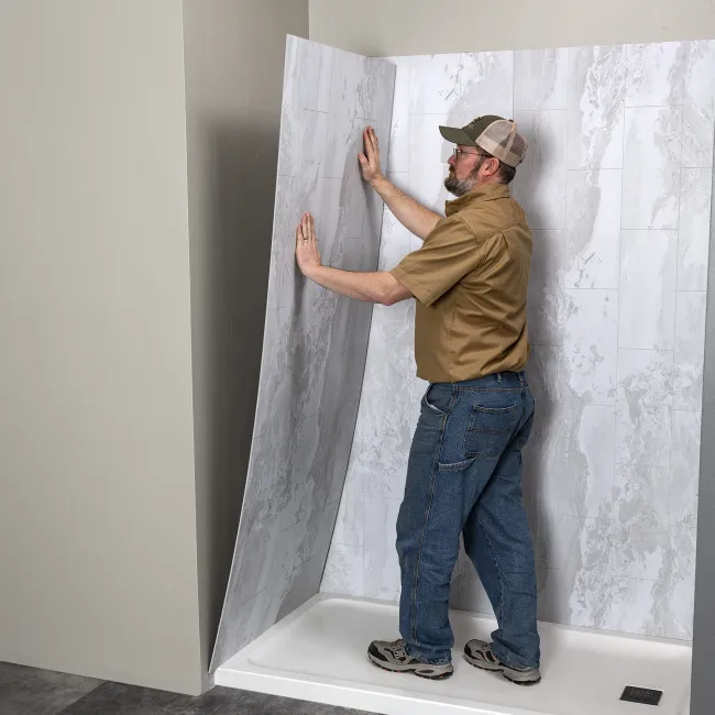 Man installing gray marble-patterned waterproof wall panels in a shower stall with a white base.