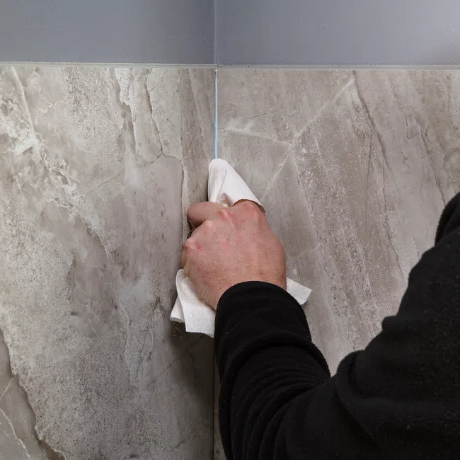 Person cleaning corner grout between large beige marble tiles with a white cloth.