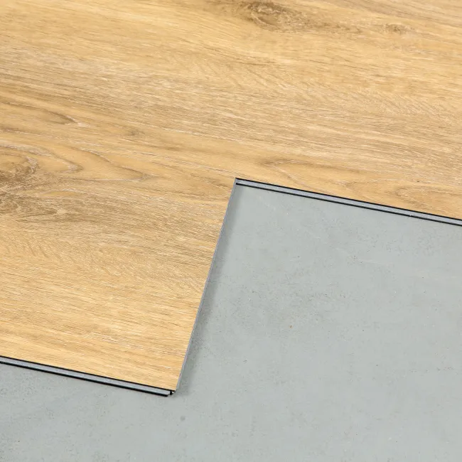Close-up of light wood laminate flooring panel partially installed over concrete subfloor.