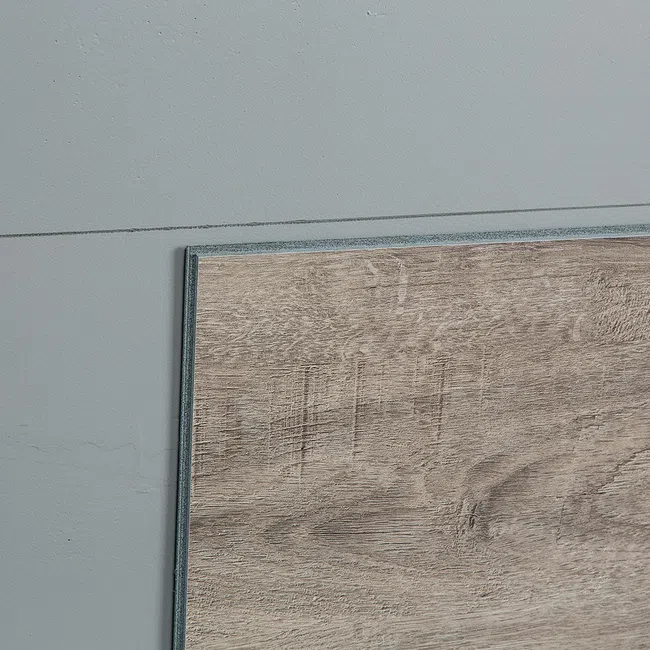 Close-up of a wooden floor panel placed on a gray concrete floor showing texture and grain details.