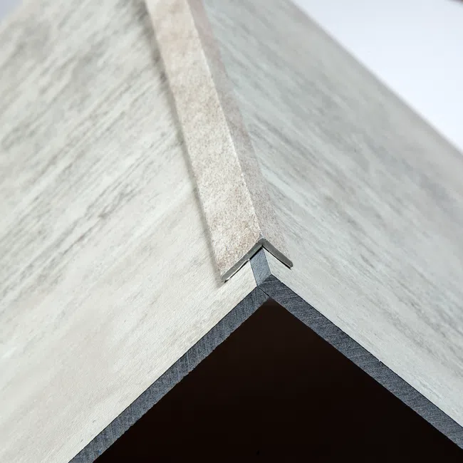 Close-up of a corner joint with a metal edge trim between two textured light gray panels forming a sharp angle.