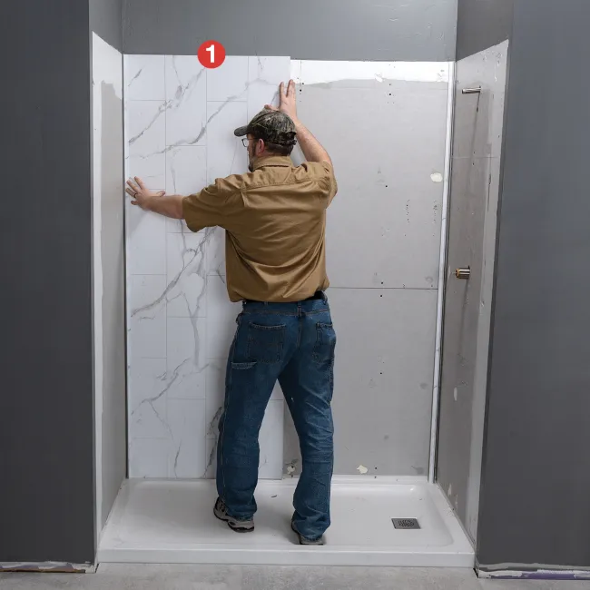 Man installing large white marble-patterned wall tiles in a shower area during renovation.