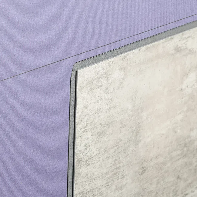 Close-up of a textured gray tile partially covering a purple fabric surface with a diagonal line.