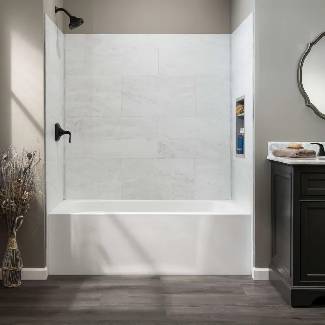 Modern bathroom with white bathtub, large gray tiles, black faucet, and dark vanity with decorative mirror.