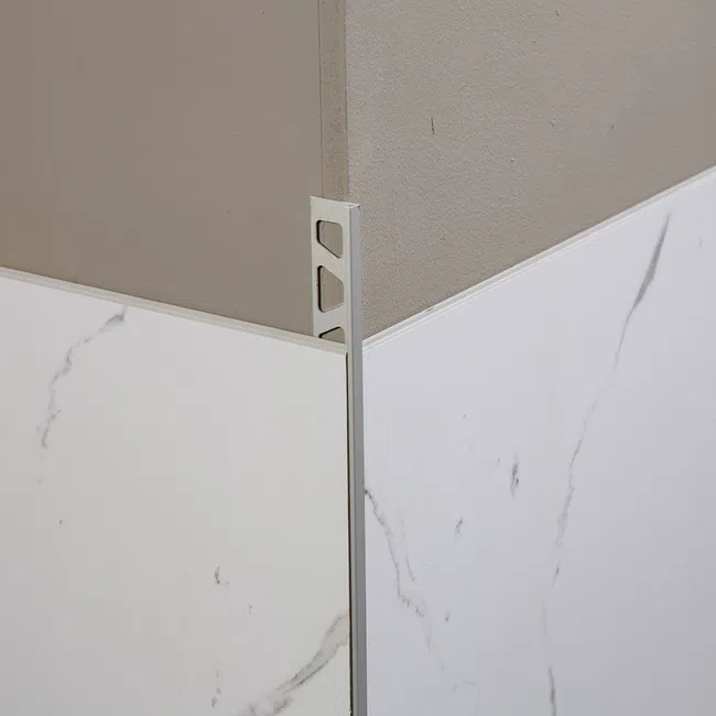 Close-up of corner edge trim installed on marble-patterned wall tiles with light gray painted wall above.