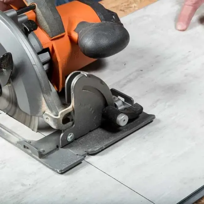 Close-up of a circular saw cutting a tile with an orange handle and black grip on a work surface.