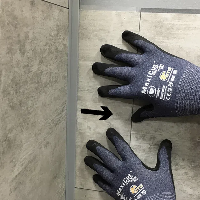 Pair of black and gray MaxiCut safety gloves on tiled floor with black arrow pointing between them